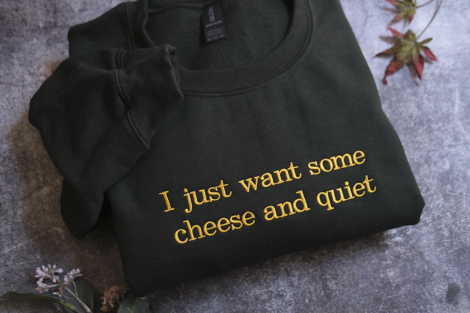 A black sweatshirt with yellow text that says "I just want some cheese and quiet" is displayed on a gray surface.