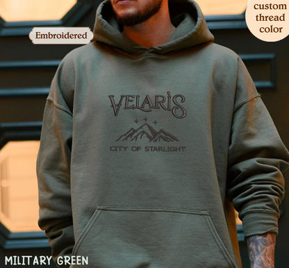 A person wearing a green hoodie with the text "VELARI'S CITY OF STARLIGHT" printed on it.