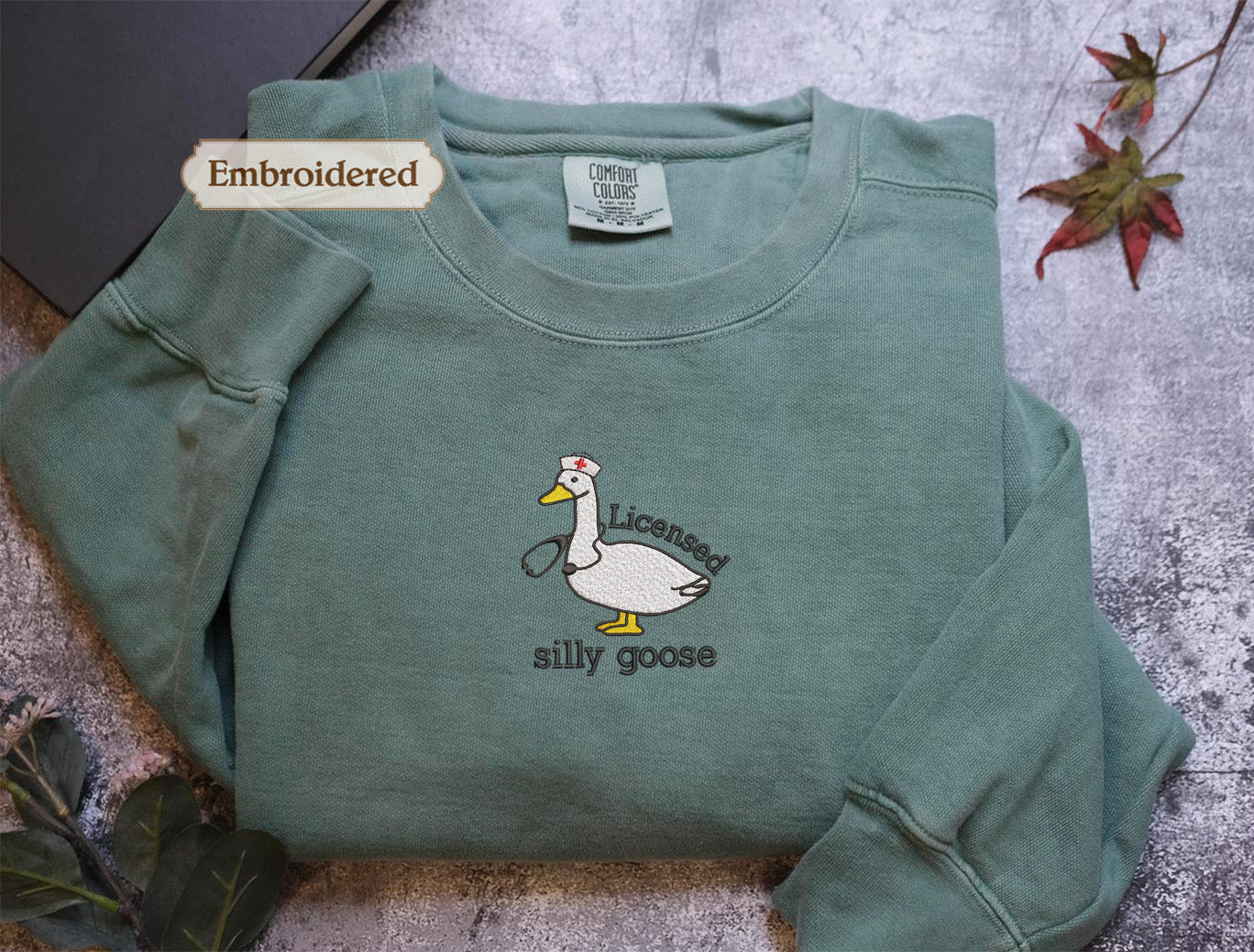 a green long-sleeved shirt with a cartoon duck and the text "Licenced silly goose" embroidered on it.