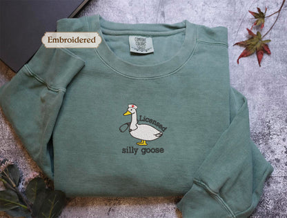 a green long-sleeved shirt with a cartoon duck and the text "Licenced silly goose" embroidered on it.