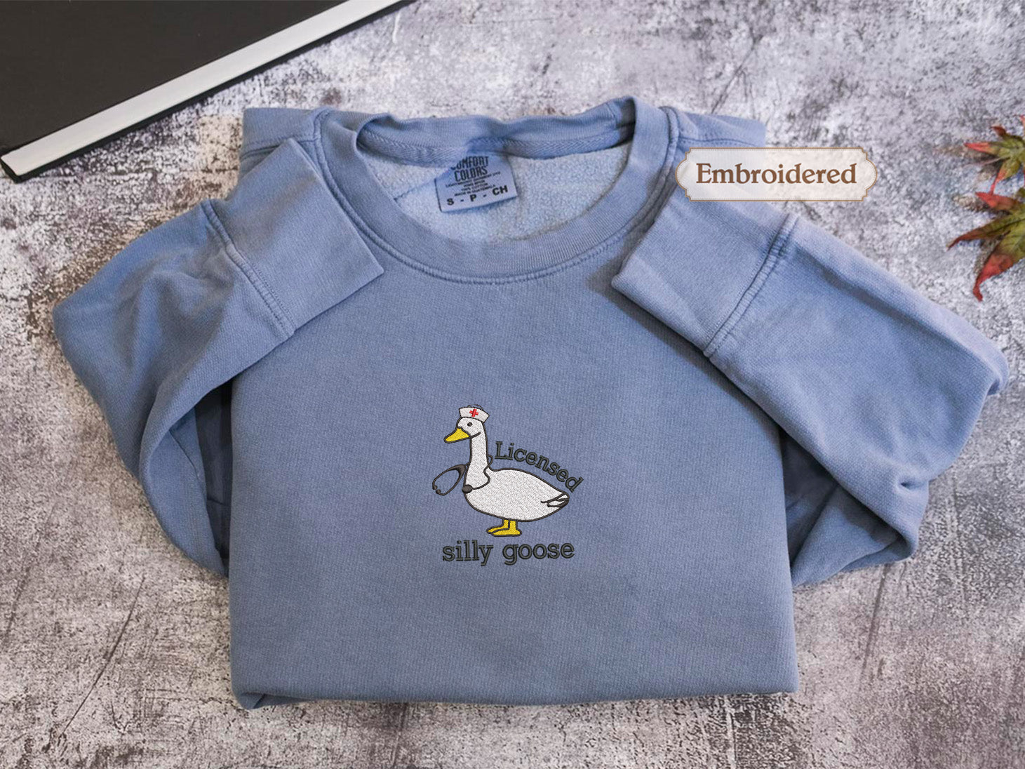 A blue long-sleeved shirt with a cartoon goose and the text "LICENSED silly goose" embroidered on it.