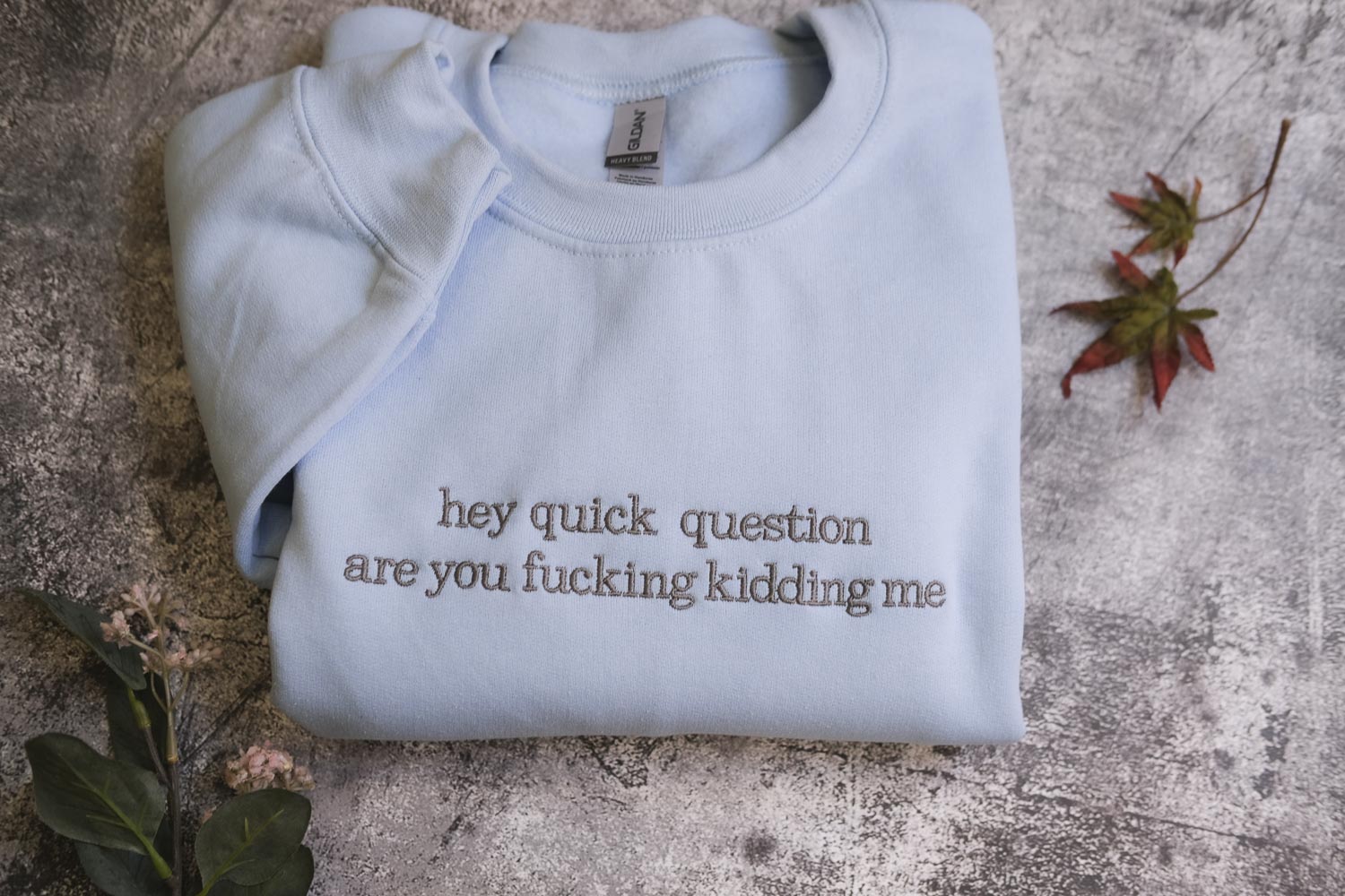 a light blue t-shirt with the text "hey quick question are you fucking Kiddin Me" printed on it, along with some leaves and flowers on the surface.