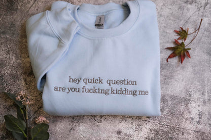 a light blue t-shirt with the text "hey quick question are you fucking Kiddin Me" printed on it, along with some leaves and flowers on the surface.