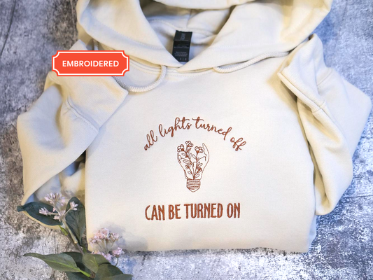 A white hoodie with the text "all lights turned off can be turned on" printed on it, along with an illustration of a light bulb.
