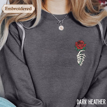 A person wearing a gray sweatshirt with a red rose embroidered on the front, along with a necklace and a pendant.