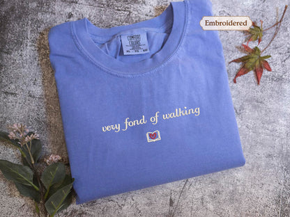 A blue t-shirt with the text "very fond of walking" printed on it, along with a small embroidered label and a leaf.
