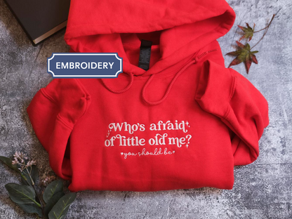 A red hoodie with white text is displayed on a gray surface, accompanied by a black book and some leaves.