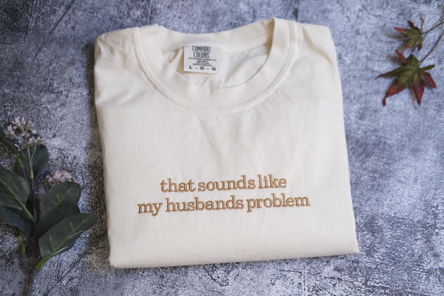 A white t-shirt with the text "that sounds like my husband's problem" printed on it, along with a small label on the collar.