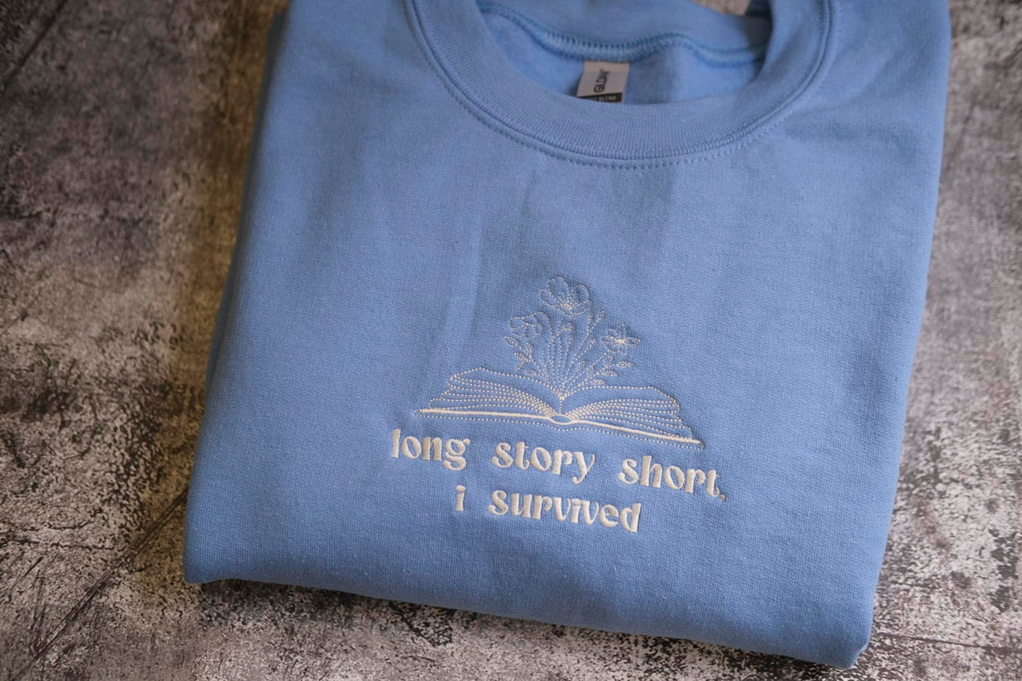 A light blue t-shirt with a white embroidered design and text on it.