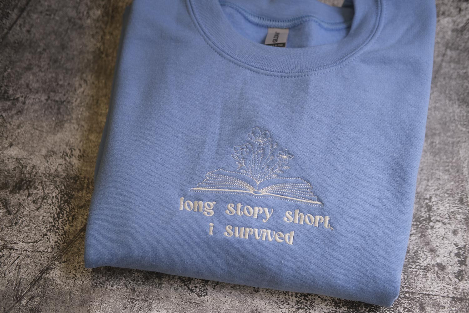 A light blue t-shirt with a white embroidered design and text on it.