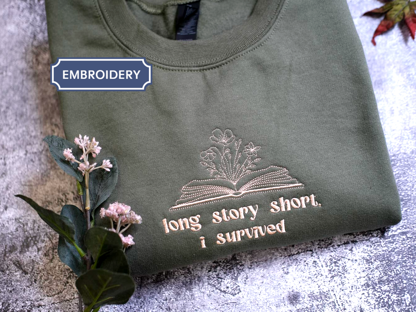 A green t-shirt with a printed design and text, along with some flowers and leaves, on a textured surface.