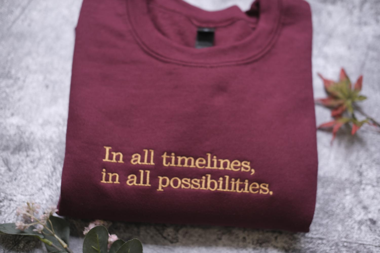A maroon t-shirt with the text "In all timelines, in all possibilities" printed on it, along with a small leaf and a plant.