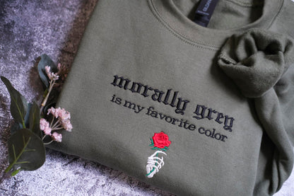 A gray sweatshirt with the text "morally grey is my favorite color" and a red rose embroidered on it, along with a skeleton hand holding the rose.