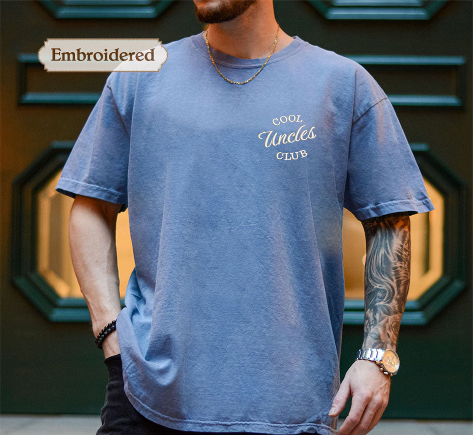 A man wearing a blue t-shirt with the text "Cool Uncle's Club" embroidered on it, standing in front of a green door.