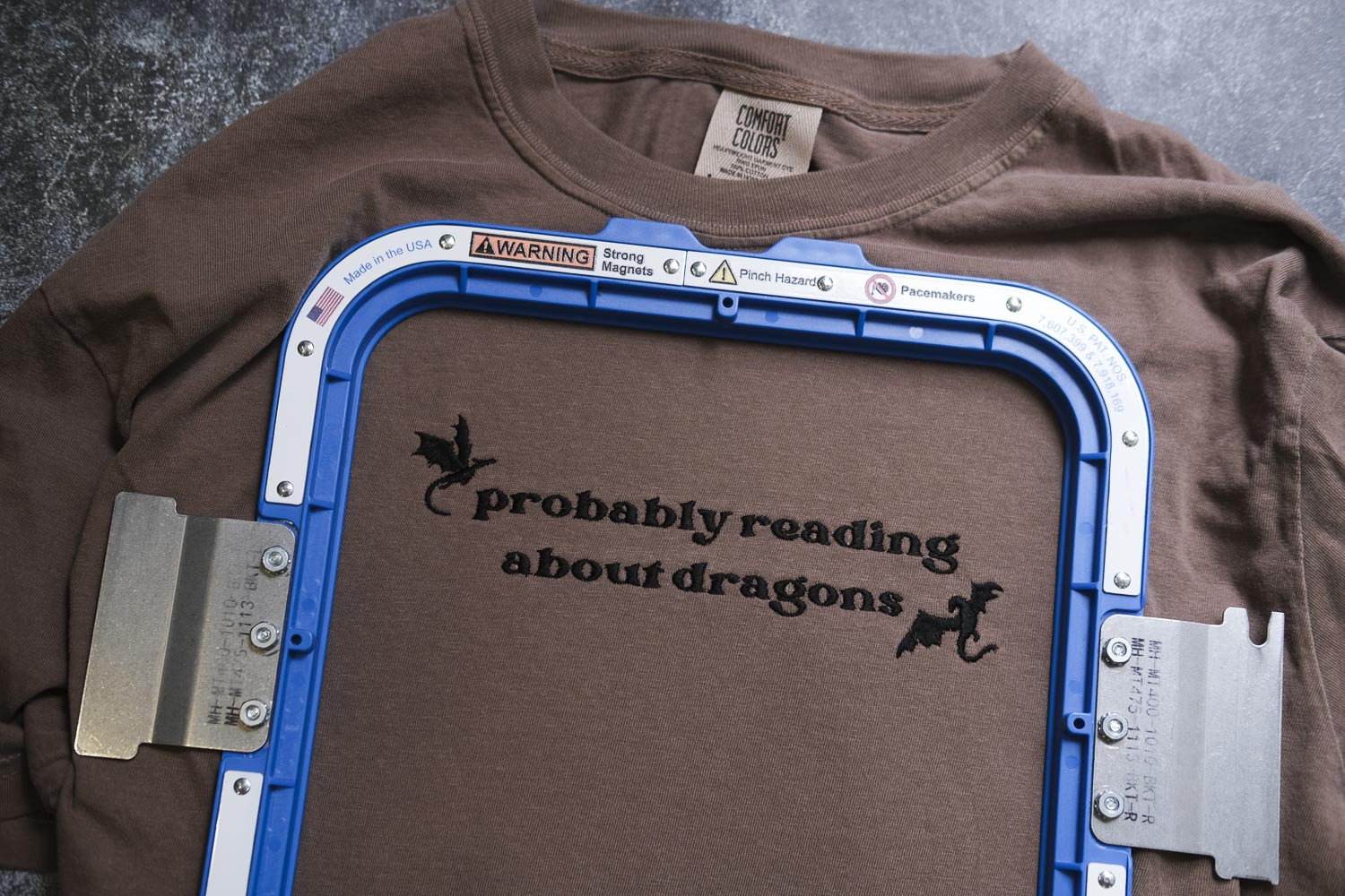 A brown t-shirt with a blue frame and the text "probably reading about dragons" printed on it.