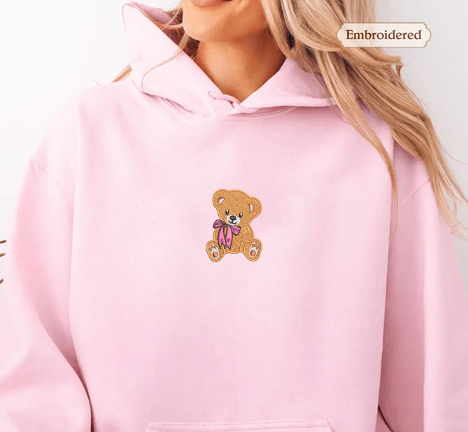 A woman wearing a pink hoodie with a teddy bear embroidered on it.