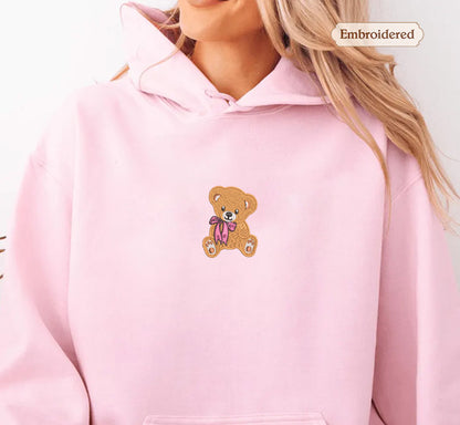 A woman wearing a pink hoodie with a teddy bear embroidered on it.