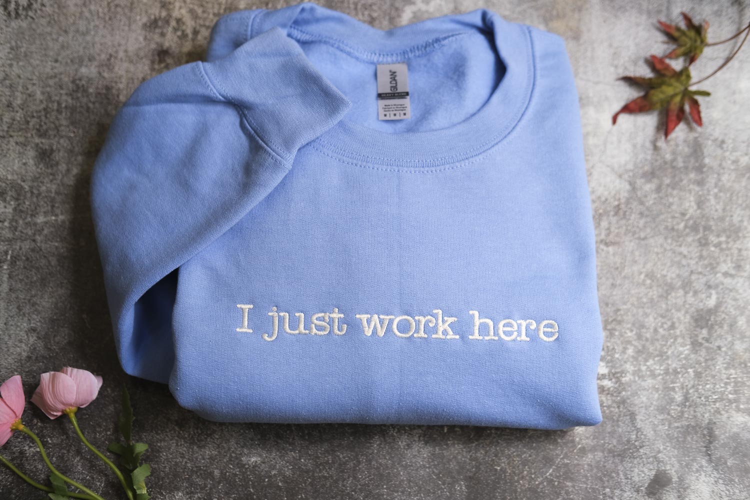 A blue t-shirt with the text "I just work here" printed on it, along with some flowers and a leaf in the background.