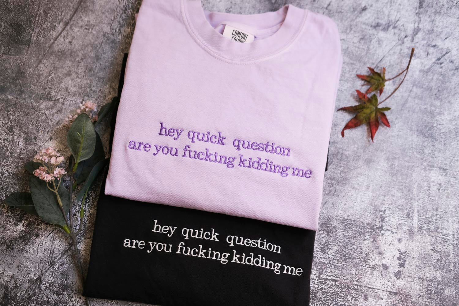a pair of t-shirts with text printed on them, placed on a gray surface.