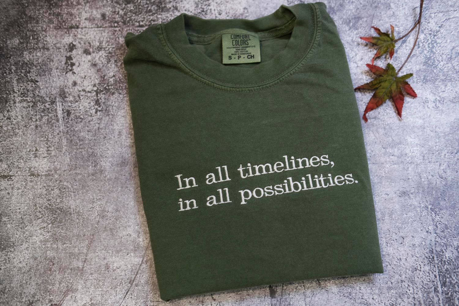 A green t-shirt with the text "In all timelines, in all possibilities" printed on it, along with a small label on the collar.