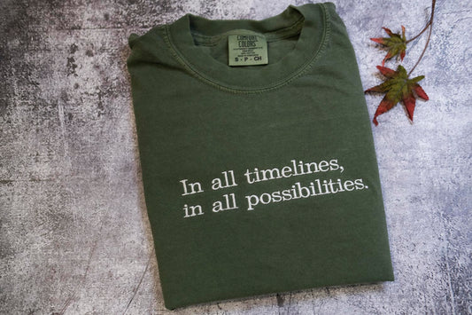 A green t-shirt with the text "In all timelines, in all possibilities" printed on it, along with a small label on the collar.