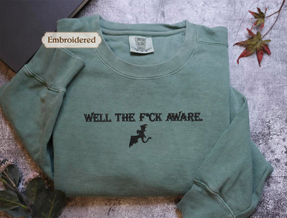 a green long-sleeved shirt with the text "WELL THE F*CK AWARE" printed on it.