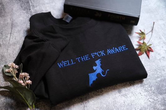 a black t-shirt with blue text and a graphic design, along with a book and some flowers on a gray surface.