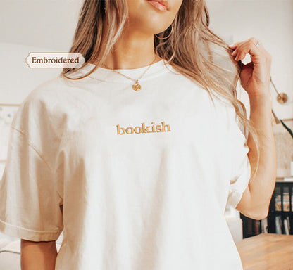 A woman wearing a white t-shirt with the word "bookish" embroidered on it, posing with her hair in her hand.