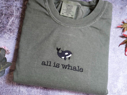 a gray t-shirt with a black and white whale embroidered on it, along with the text &quot;all is whale&quot; printed on the front.