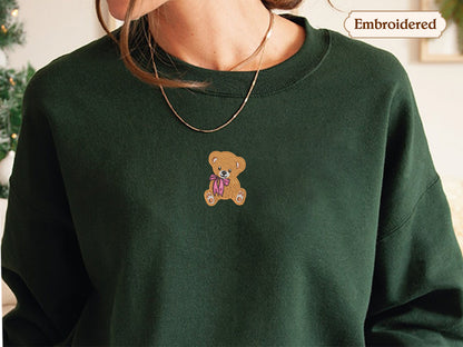 A close-up of a person wearing a green sweater with a teddy bear embroidered on it.