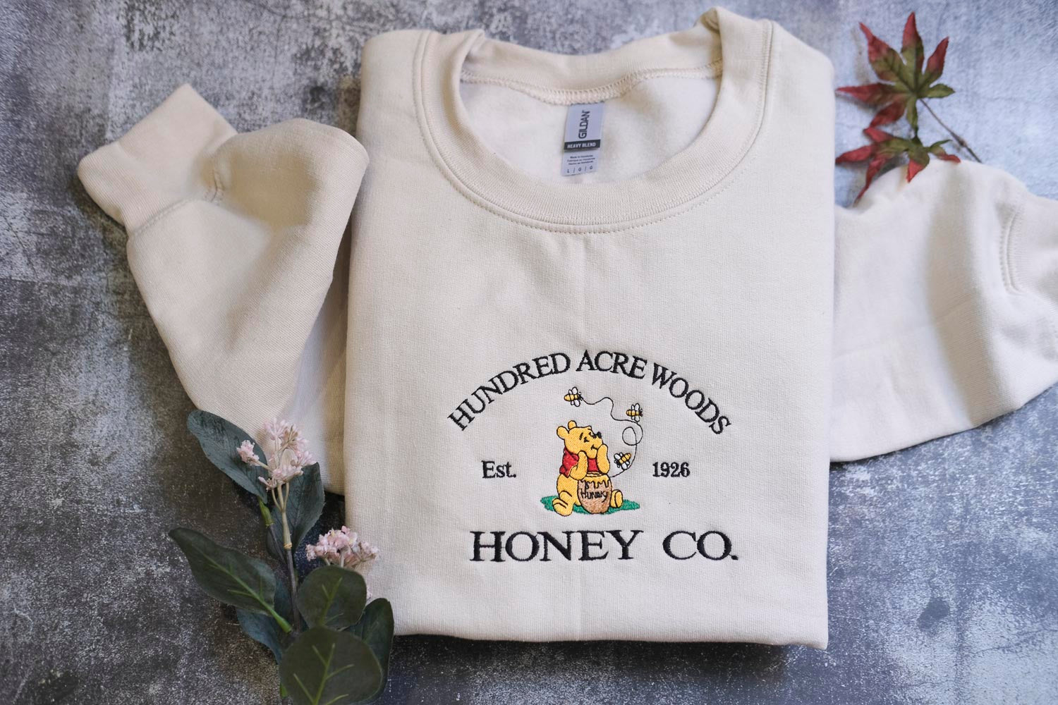 A white sweatshirt with a logo and text printed on it, along with some leaves and flowers.