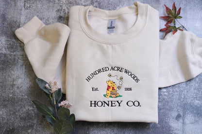 A white sweatshirt with a logo and text printed on it, along with some leaves and flowers.