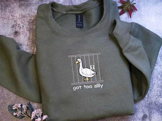 A green sweatshirt with a graphic of a duck in a cage and the text "got too silly" printed on it.