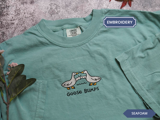 A light green t-shirt with a graphic design of two ducks and the text "Goose Bumps" printed on it.