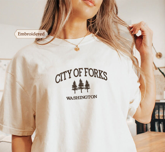 A woman wearing a white t-shirt with the text "CITY OF FORKS WASHINGTON" printed on it.