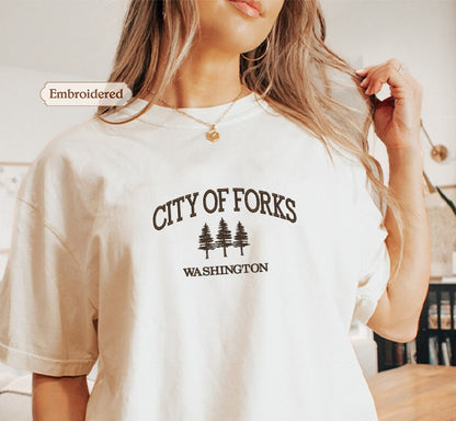 A woman wearing a white t-shirt with the text "CITY OF FORKS WASHINGTON" printed on it.