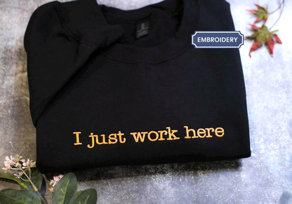 a black t-shirt with the text "I just work here" printed on it in orange lettering.