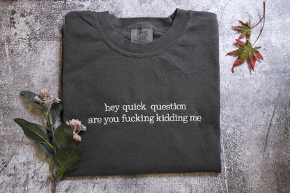 a gray t-shirt with the text "hey quick question are you fucking kidding me" printed on it, along with some leaves and flowers.