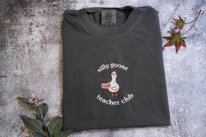 A gray t-shirt with a graphic of a goose and the text "silly goose teacher chub" printed on it, along with a small leaf and a flower.