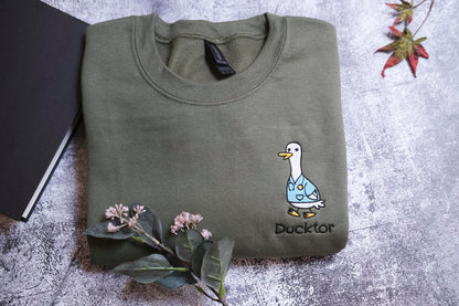 a green t-shirt with a cartoon duck and the word "Duckster" printed on it, along with a small plant and a leaf.