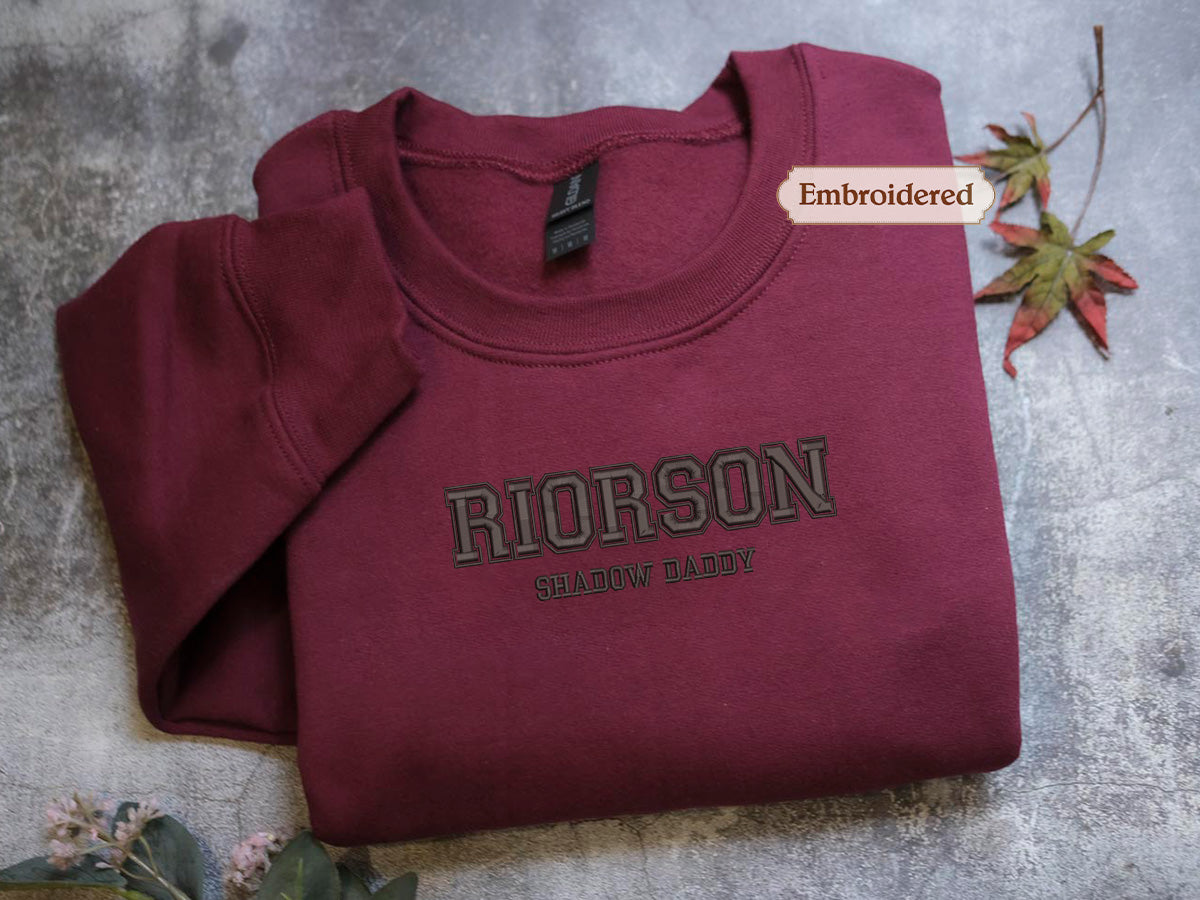 A burgundy sweatshirt with the name "RIONSON" and the phrase "SHALLOW DADDY" printed on it, along with a small embroidered label.