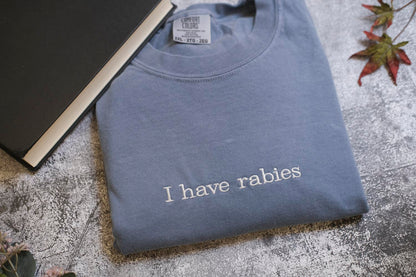 A gray t-shirt with the text "I haverabies" printed on it, along with a black book and some leaves in the background.