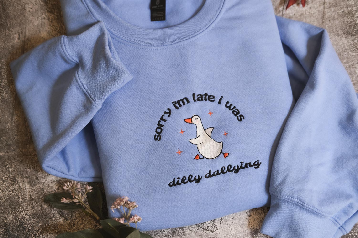 A light blue sweatshirt with a humorous text and graphic design printed on it.