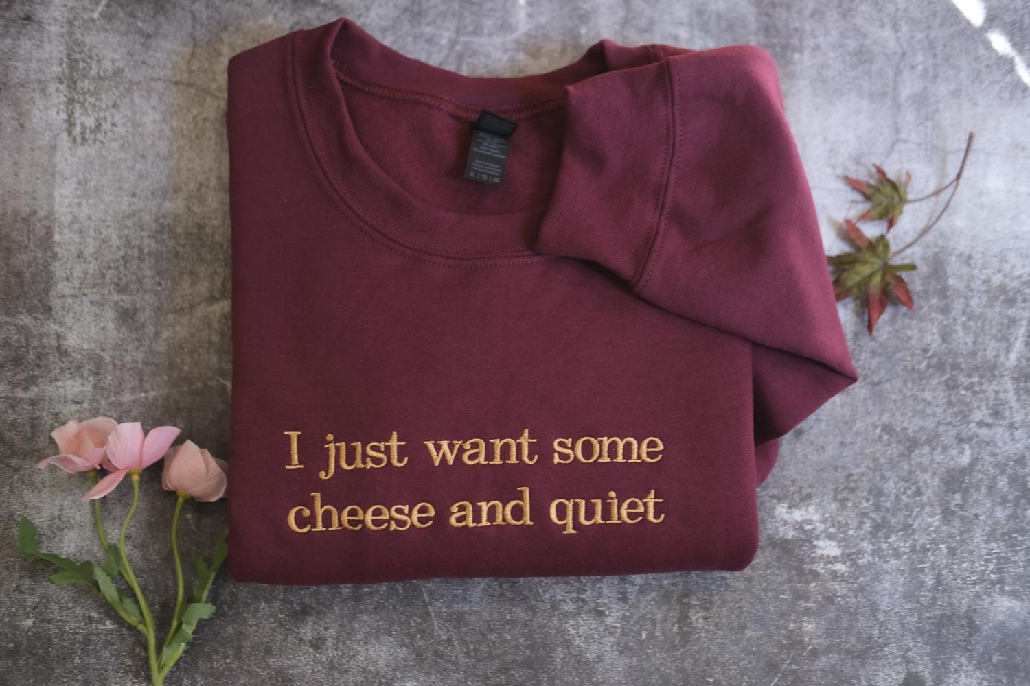 A burgundy sweatshirt with the text "I just want some cheese and quiet" printed on it, along with a small pink rose and some leaves.