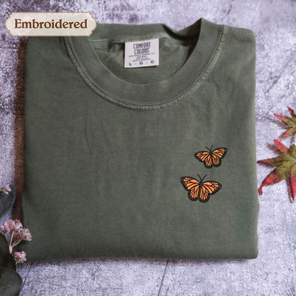 a green t-shirt with a small embroidered design of two orange butterflies on the front.