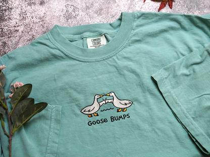 A light green t-shirt with a graphic design of two ducks and the text "Goose Bumps" printed on it.