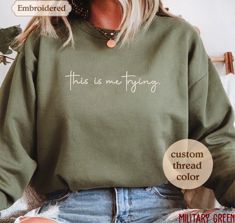 A person wearing a green sweatshirt with the text "This is me trying" printed on it.