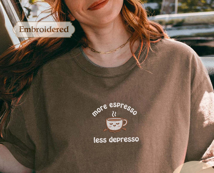 A woman wearing a brown t-shirt with a coffee cup design and text, smiling and looking at the camera.