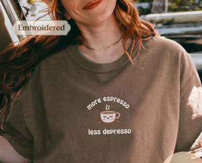 A woman wearing a brown t-shirt with a coffee cup design and text, smiling and looking at the camera.
