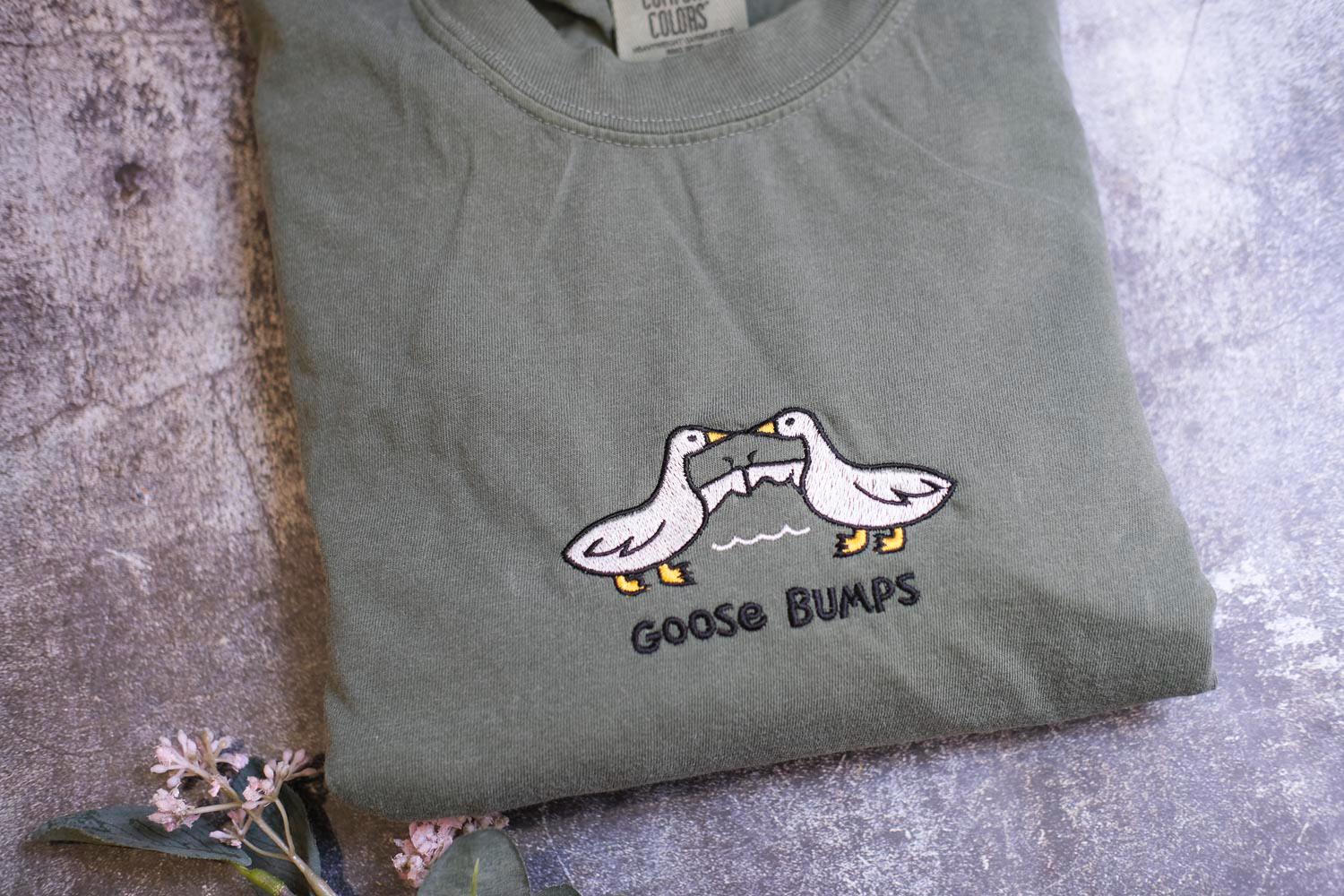 a pair of geese on a t - shirt next to a flower